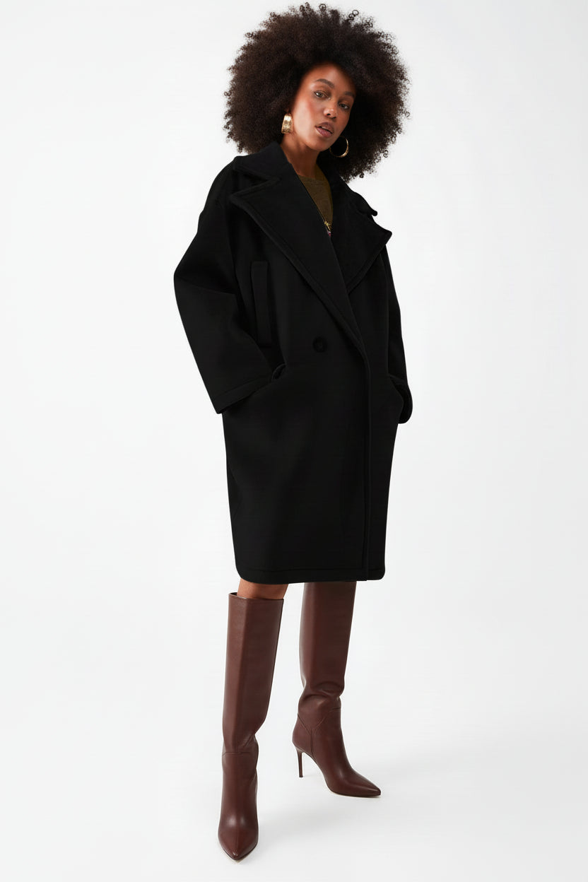 Mujer vistiendo abrigo negro extragrande de terciopelo con solapas grandes y botas altas marrones.