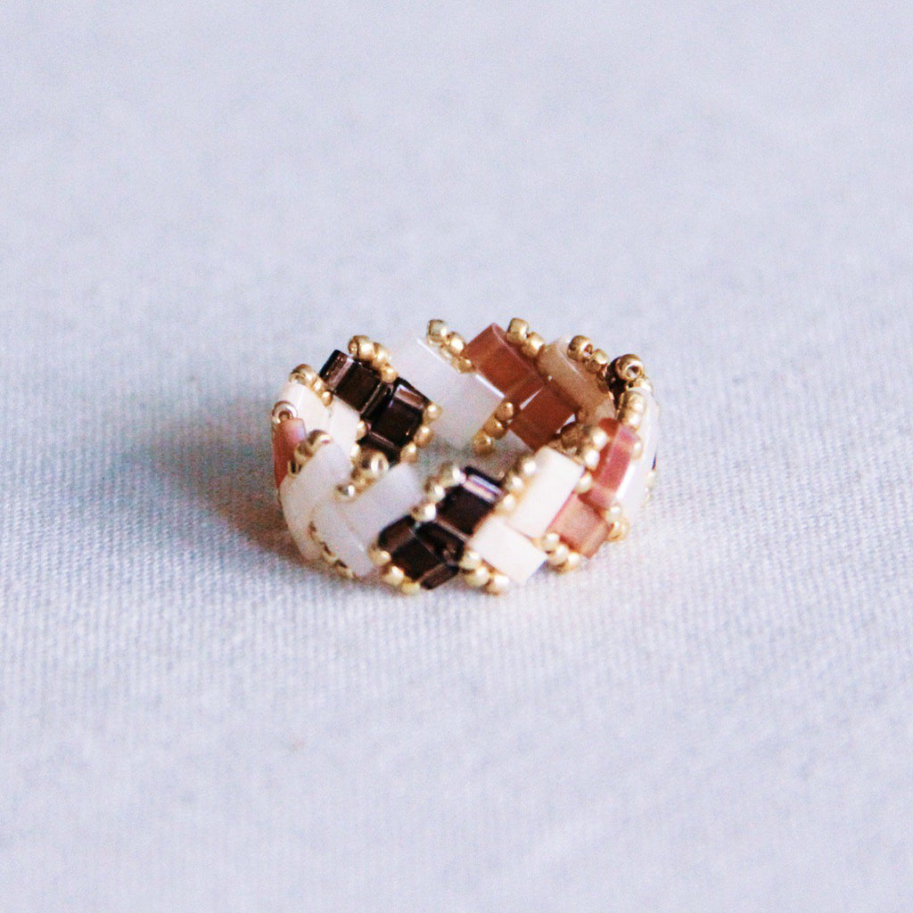 Anillo tejido con cuentas Tila cuadradas en colores marrón, beige y blanco con patrón de espiga y detalles dorados.