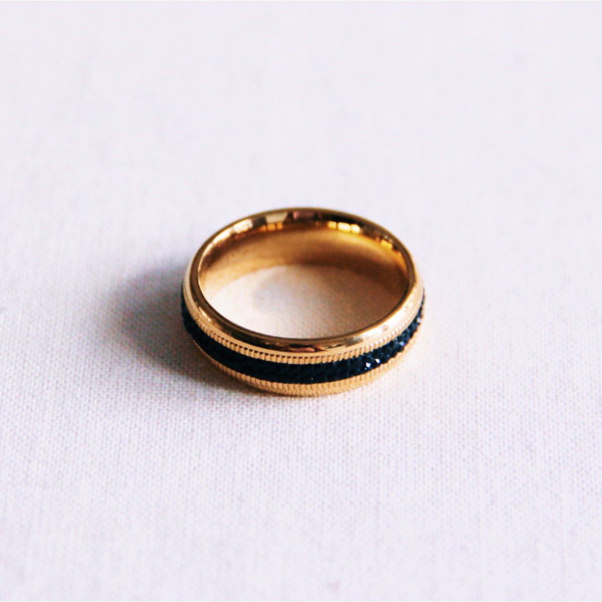 Anillo de acero inoxidable dorado con una banda central de piedras negras brillantes tipo eternity.