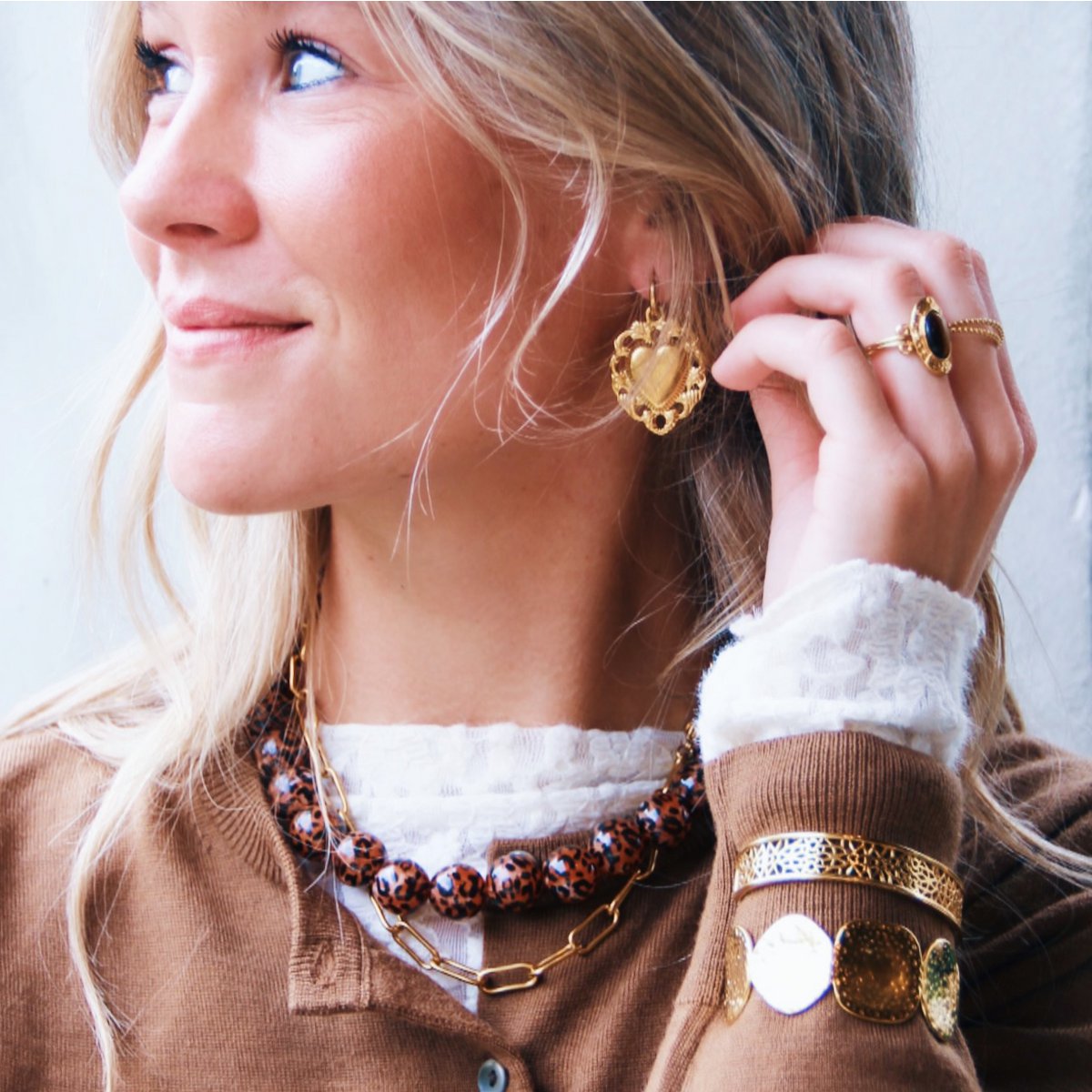 Mujer con jersey marrón y encaje llevando un anillo de ojo de tigre y pendientes grandes a juego.