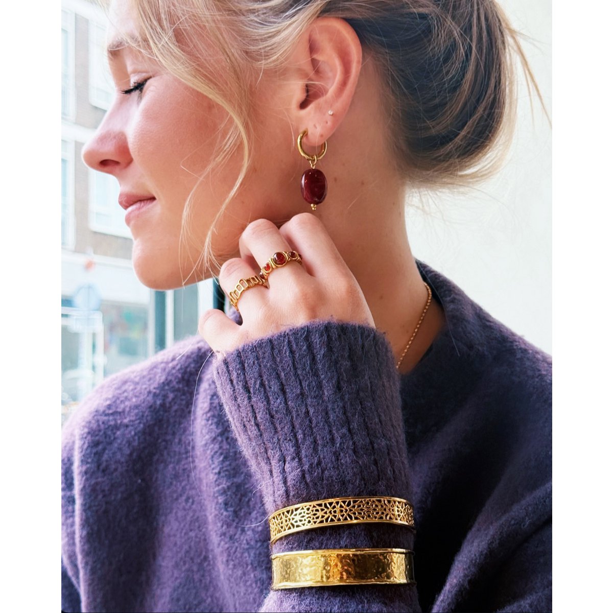 Mujer con jersey morado llevando un anillo de piedras rojas combinado con pendientes a juego y brazaletes dorados.