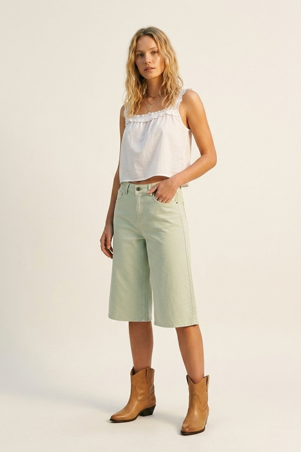 bermudas vaqueras tipo culotte en color verde menta de tiro alto, combinadas con top de tirantes blanco y botas cowboy color camel.