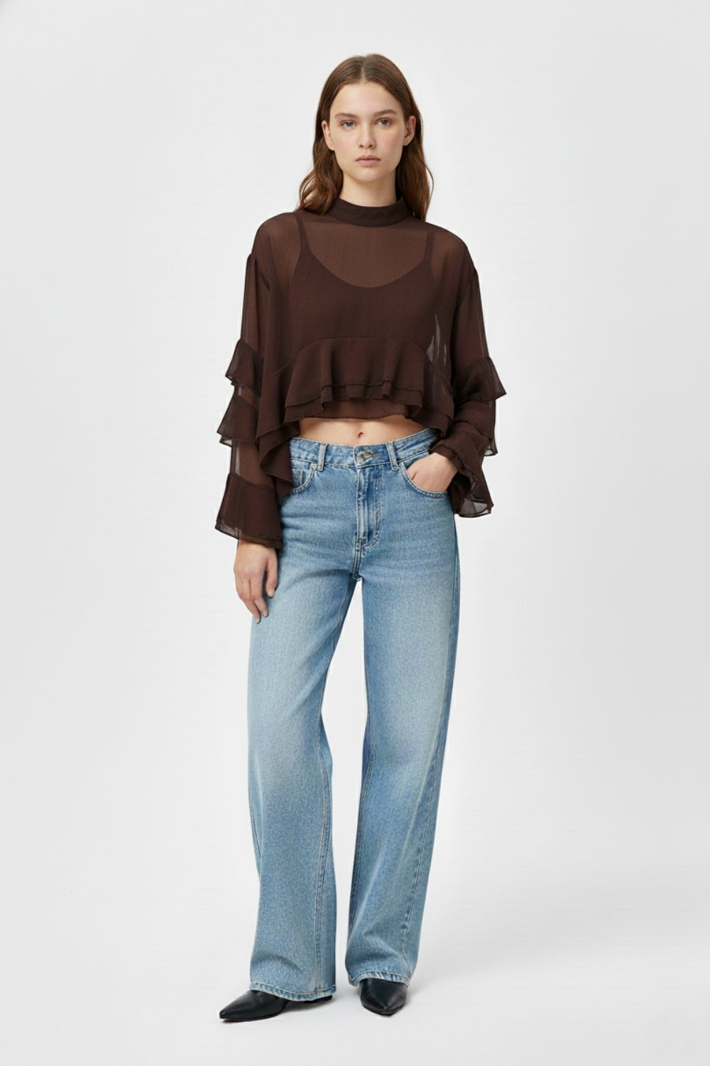 Mujer vistiendo un top corto de gasa marrón transparente con volantes asimétricos y vaqueros azules.