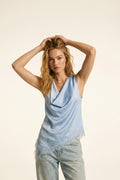 blusa azul claro de satén con cuello drapeado y bajo asimétrico de encaje floral.