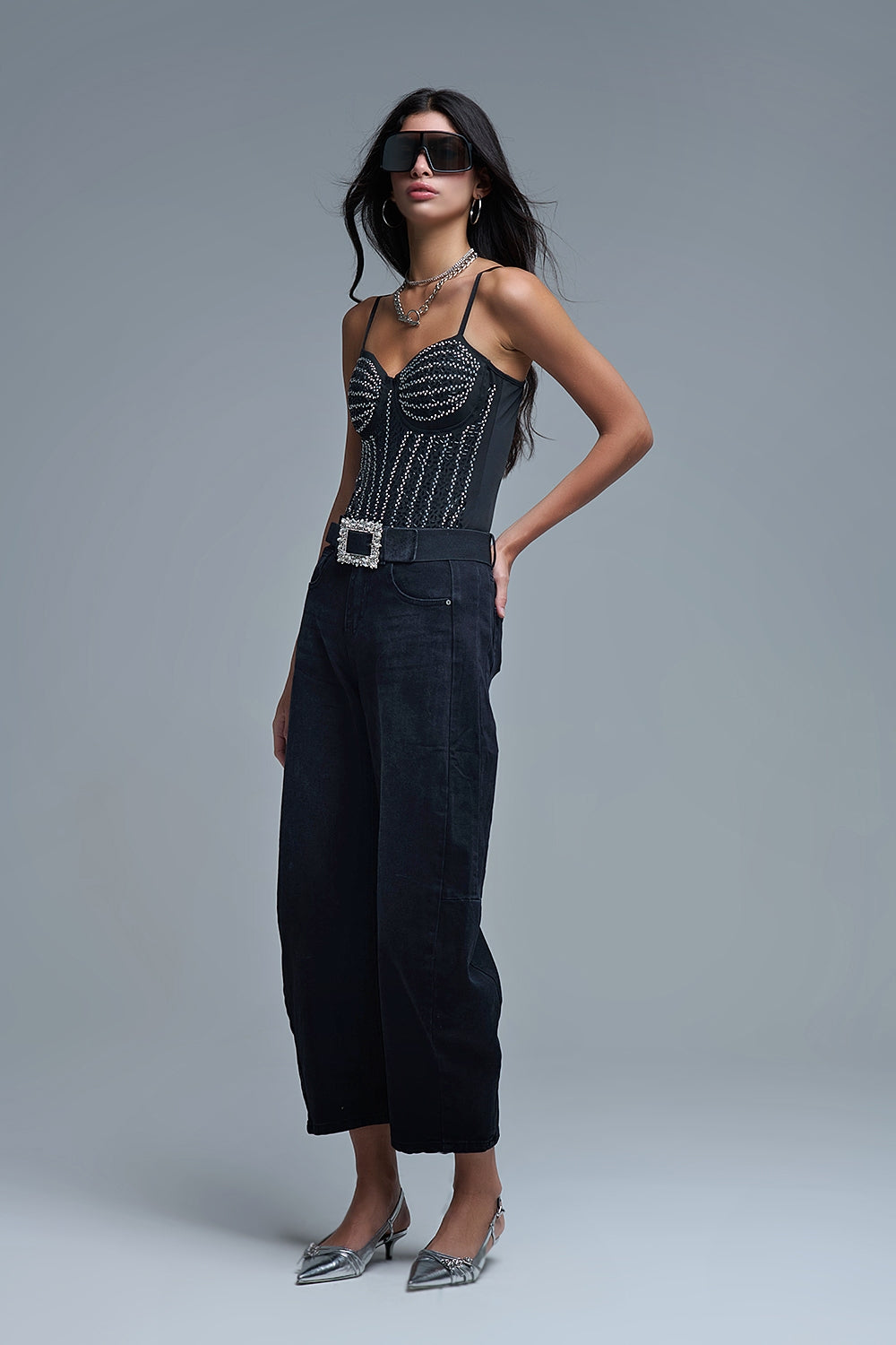 Look completo de mujer con body negro de pedrería estilo corsé, vaqueros baggy negros y zapatos plata.