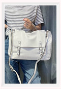 Bolso tipo cartera para mujer en color blanco con hebillas frontales y asa de mano con tachuelas.