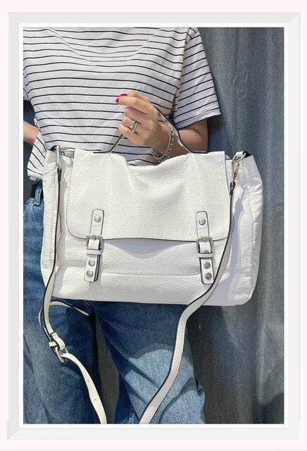 Bolso tipo cartera para mujer en color blanco con hebillas frontales y asa de mano con tachuelas.
