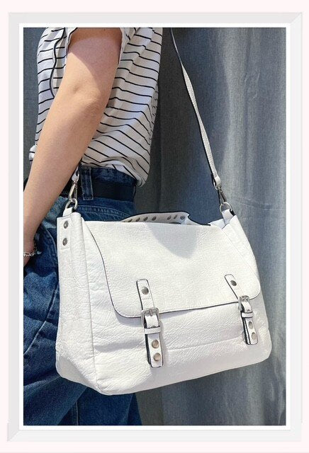 Bolso tipo cartera para mujer en color blanco con hebillas frontales y asa de mano con tachuelas.