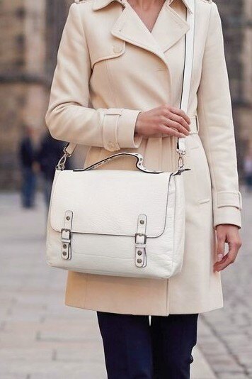 Bolso tipo cartera para mujer en color blanco con hebillas frontales y asa de mano con tachuelas.