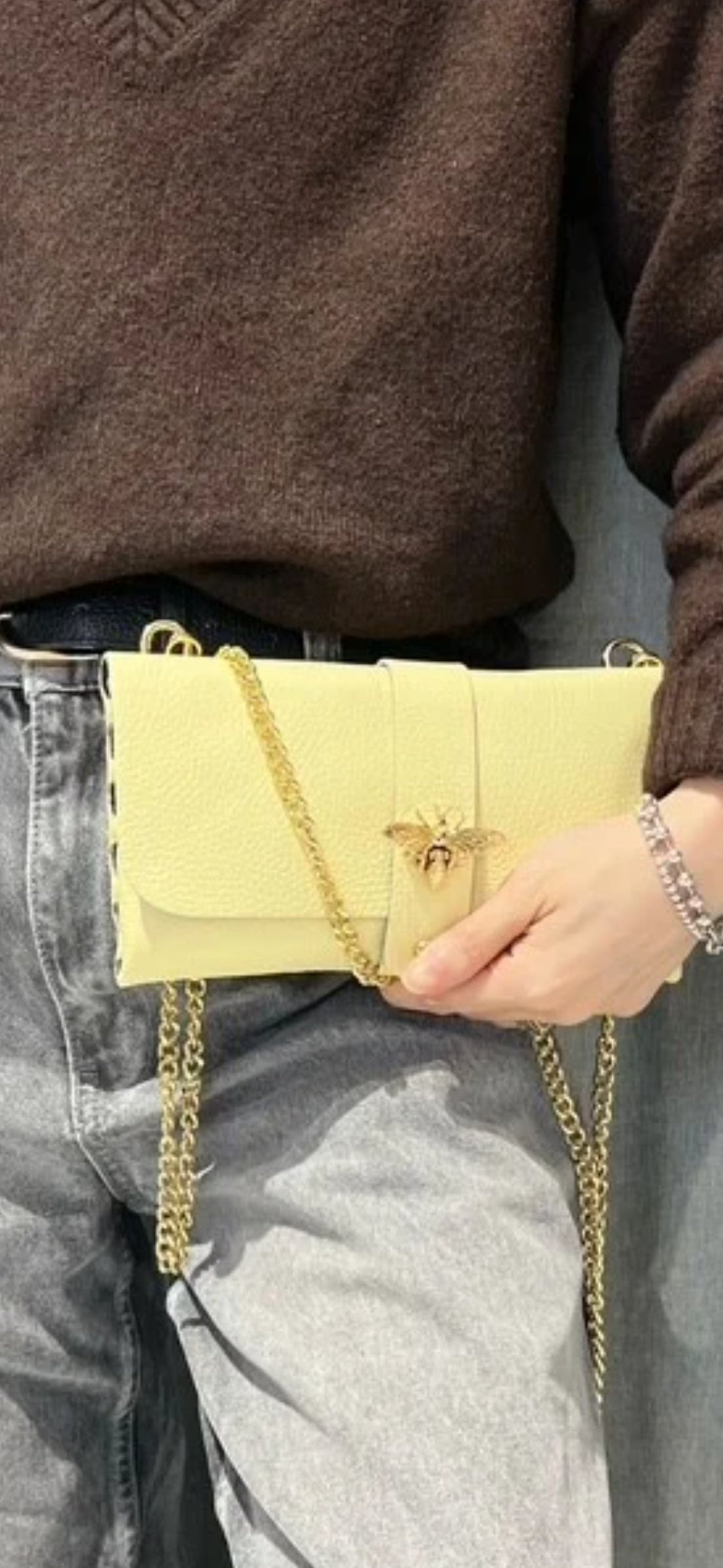 Bolso de mano tipo sobre en piel granulada amarilla con cierre de abeja dorada y cadena.