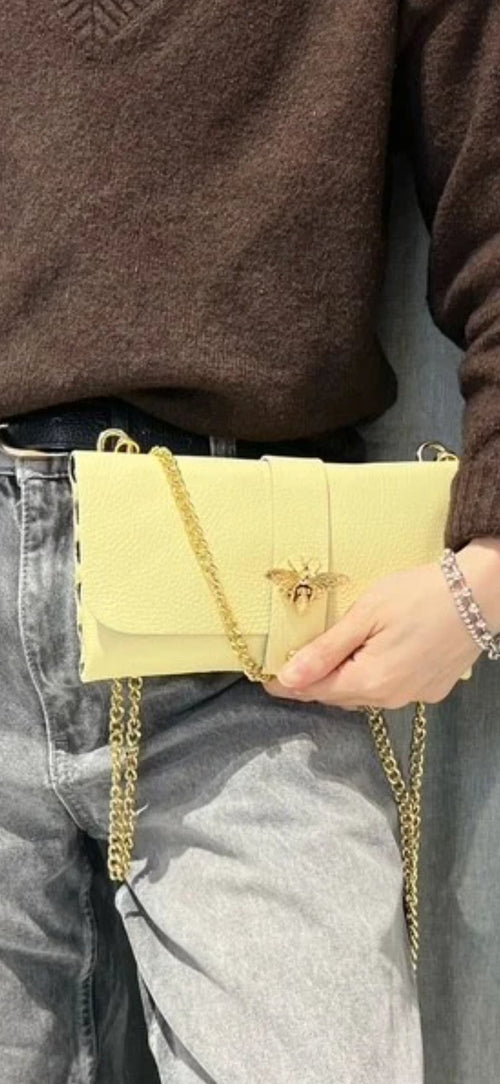 Bolso de mano tipo sobre en piel granulada amarilla con cierre de abeja dorada y cadena.