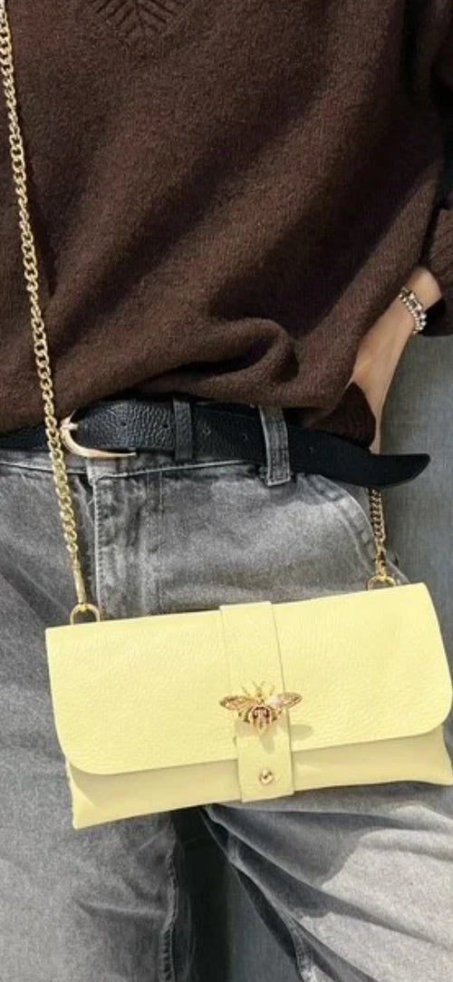 Bolso de mano tipo sobre en piel granulada amarilla con cierre de abeja dorada y cadena.