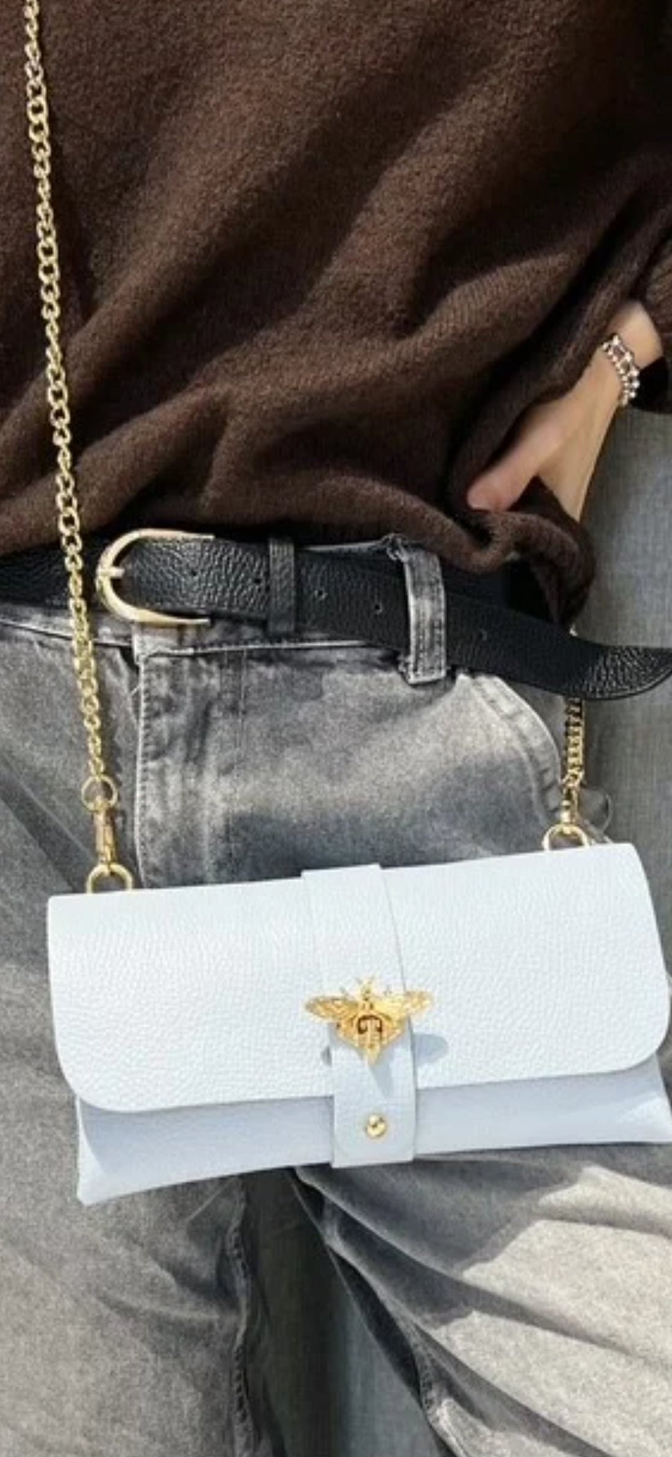 Bolso de mano tipo sobre en piel granulada azul pastel con cierre de abeja dorada y cadena.