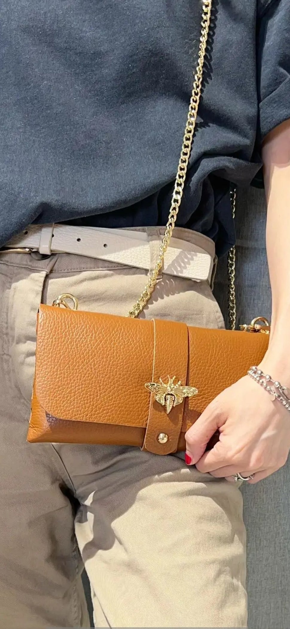Bolso de mano tipo sobre en piel granulada camel con cierre de abeja dorada y cadena.