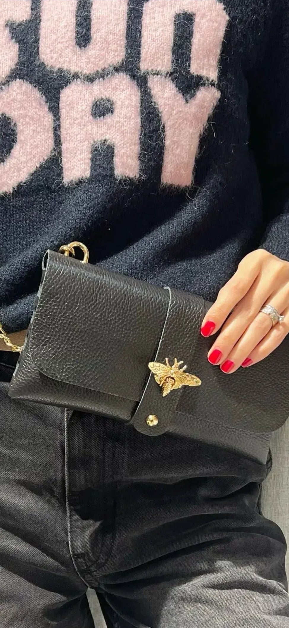 Bolso de mano tipo sobre en negra con cierre de abeja dorada y cadena.