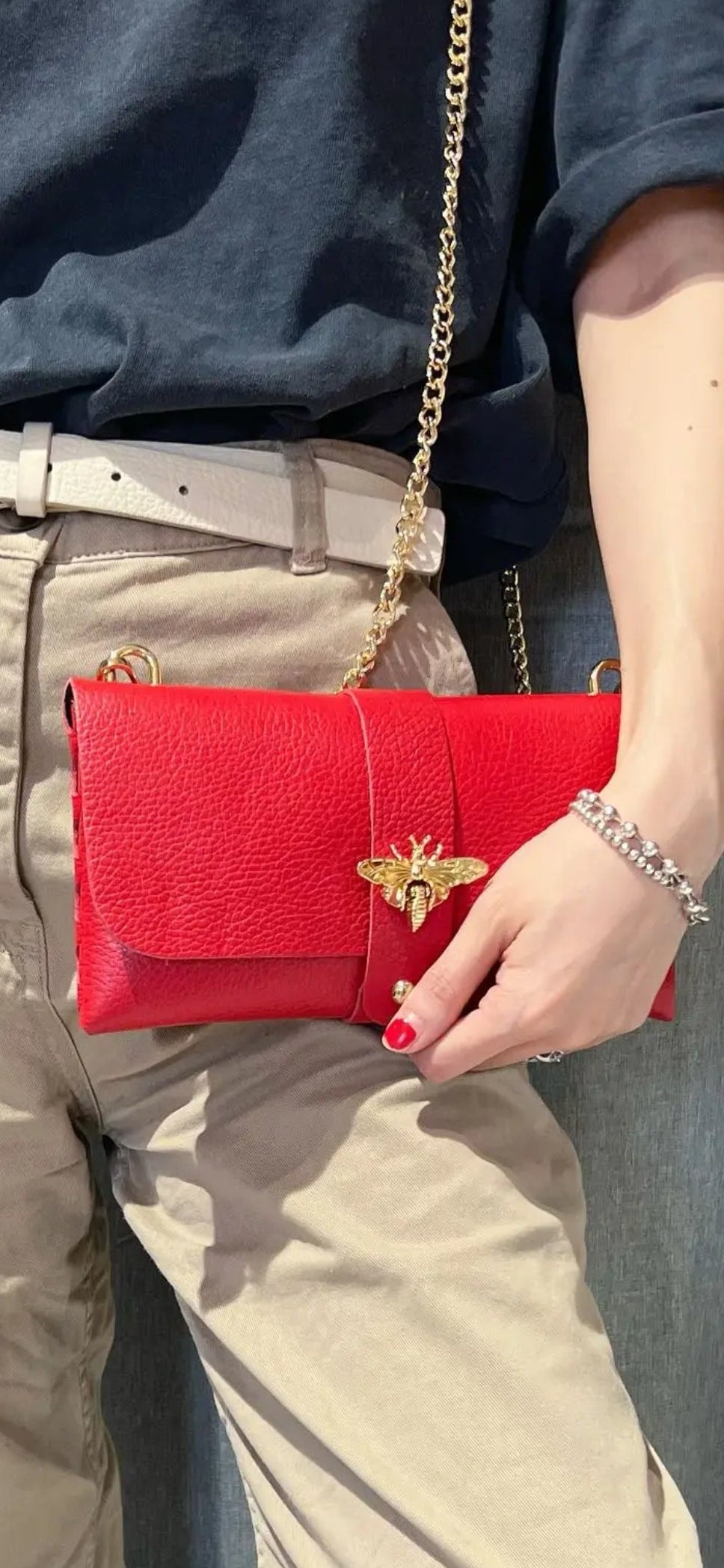 Bolso de mano tipo sobre en roja con cierre de abeja dorada y cadena.
