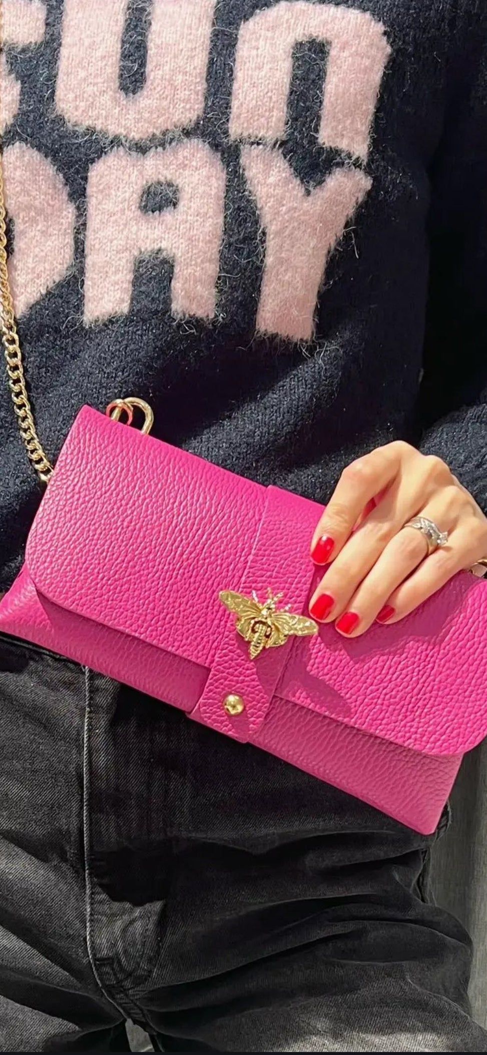 Bolso de mano tipo sobre en piel granulada rosa con cierre de abeja dorada y cadena.