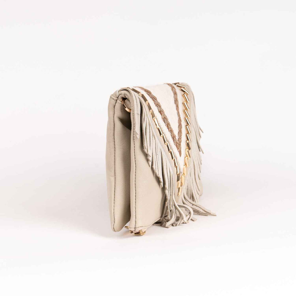 Bolso tipo clutch de estilo boho chic en piel de ante marfil, con solapa en forma de V, largos flecos, detalles trenzados metálicos y tachuelas doradas.