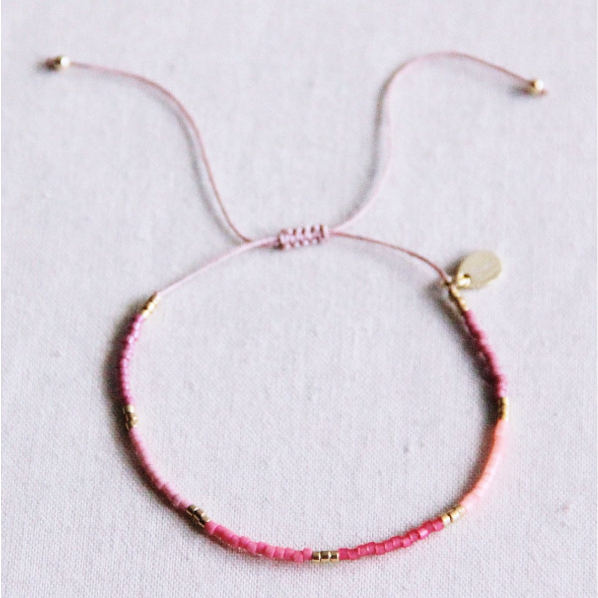 Detalle de pulsera de hilo rosa con cierre ajustable de nudos y cuentas pequeñas Miyuki.