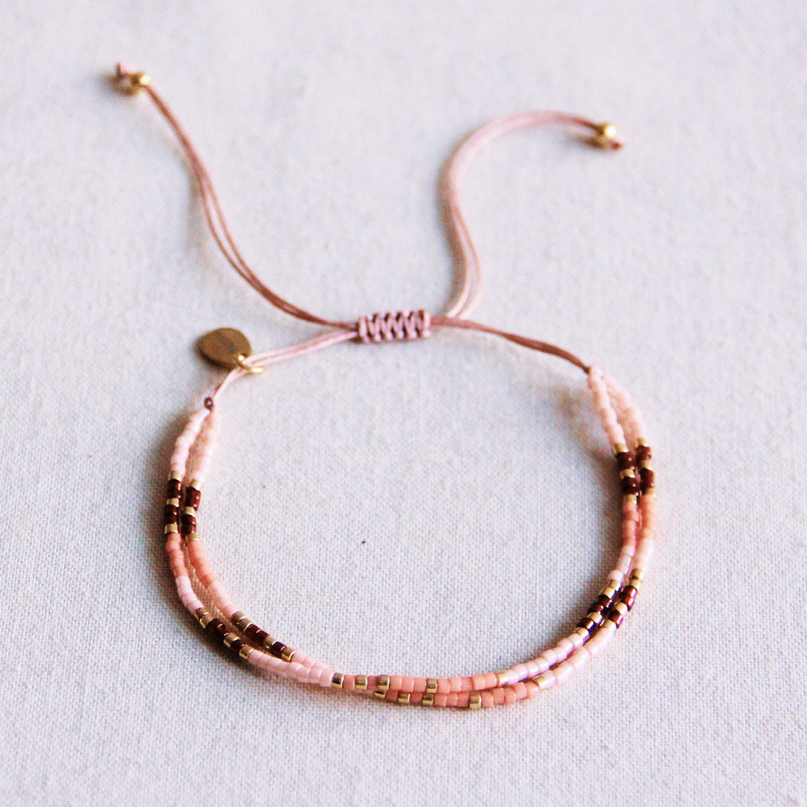 Detalle de pulsera doble de hilo rosa con cierre ajustable de nudos y cuentas pequeñas de colores.