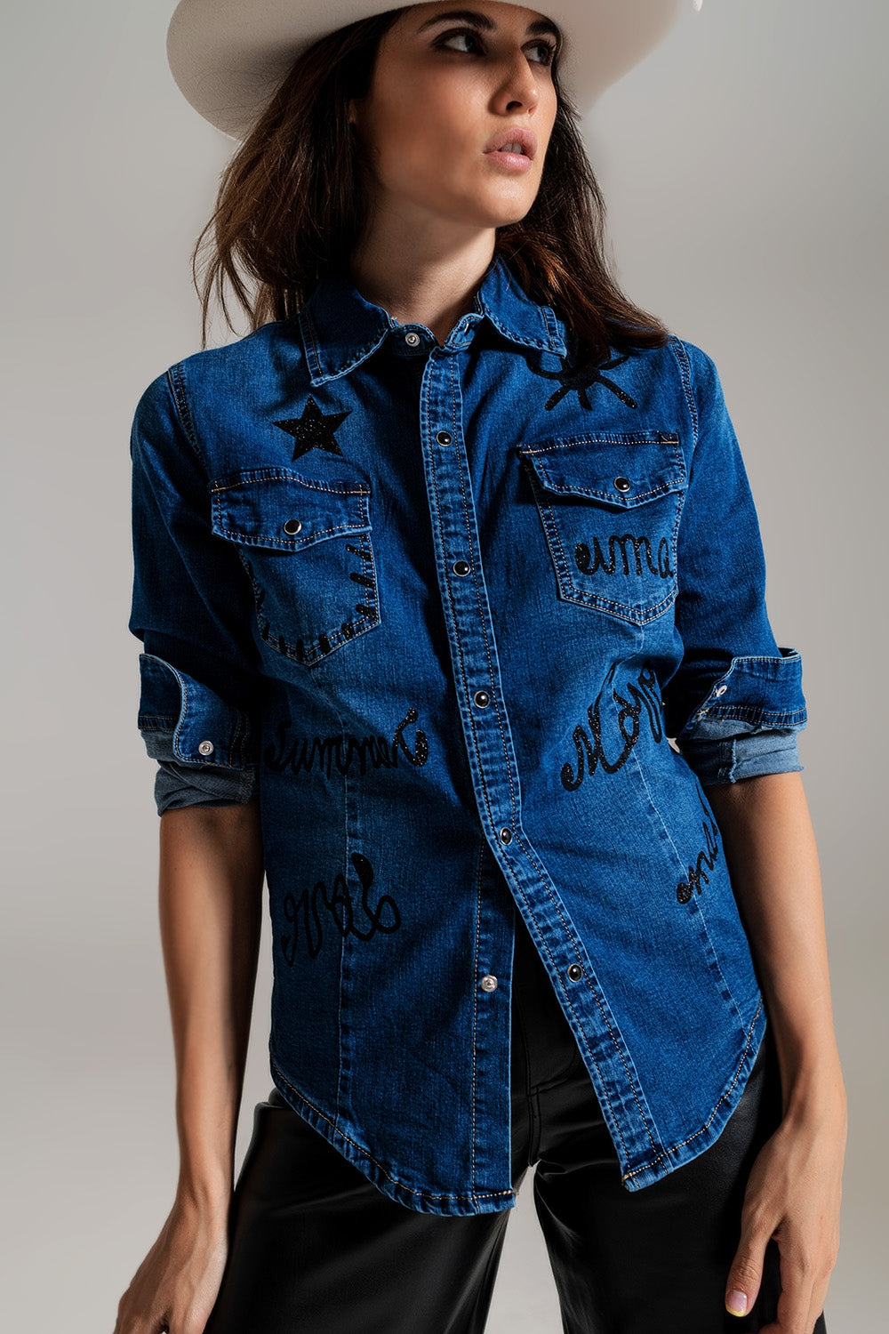 Modelo con camisa vaquera ajustada de color oscuro con detalles de strass en los hombros.