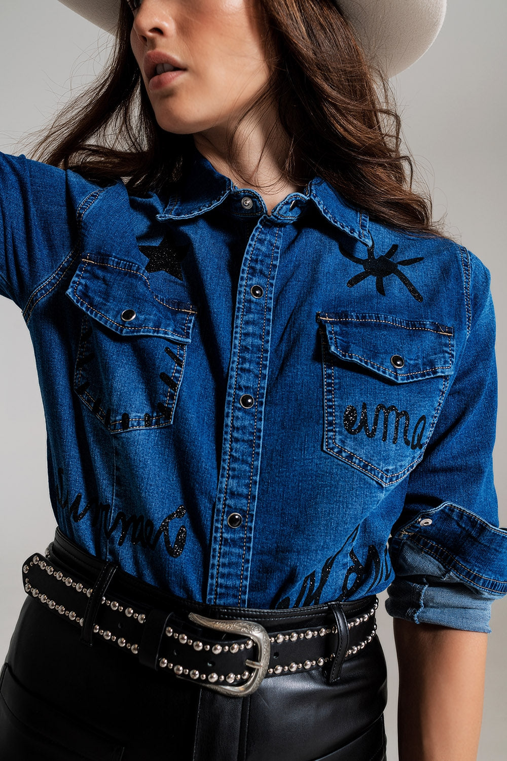 Modelo con camisa vaquera ajustada de color oscuro con detalles de strass en los hombros.