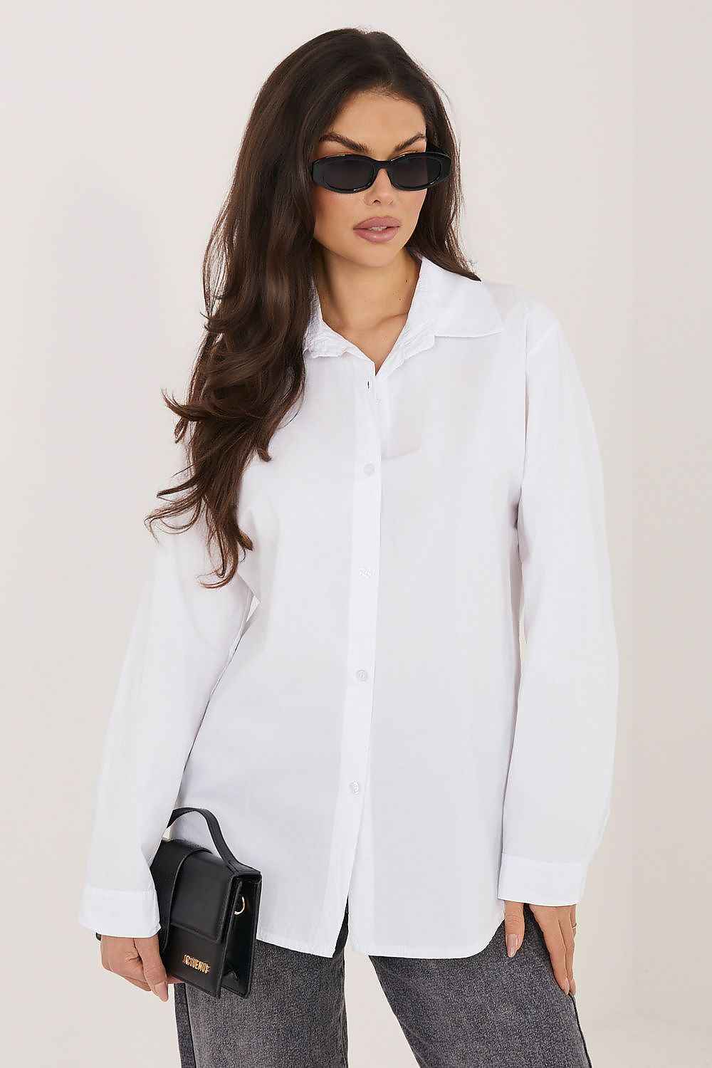 Modelo con camisa blanca de algodón 100%, gafas de sol negras y bolso de mano negro sobre fondo neutro.