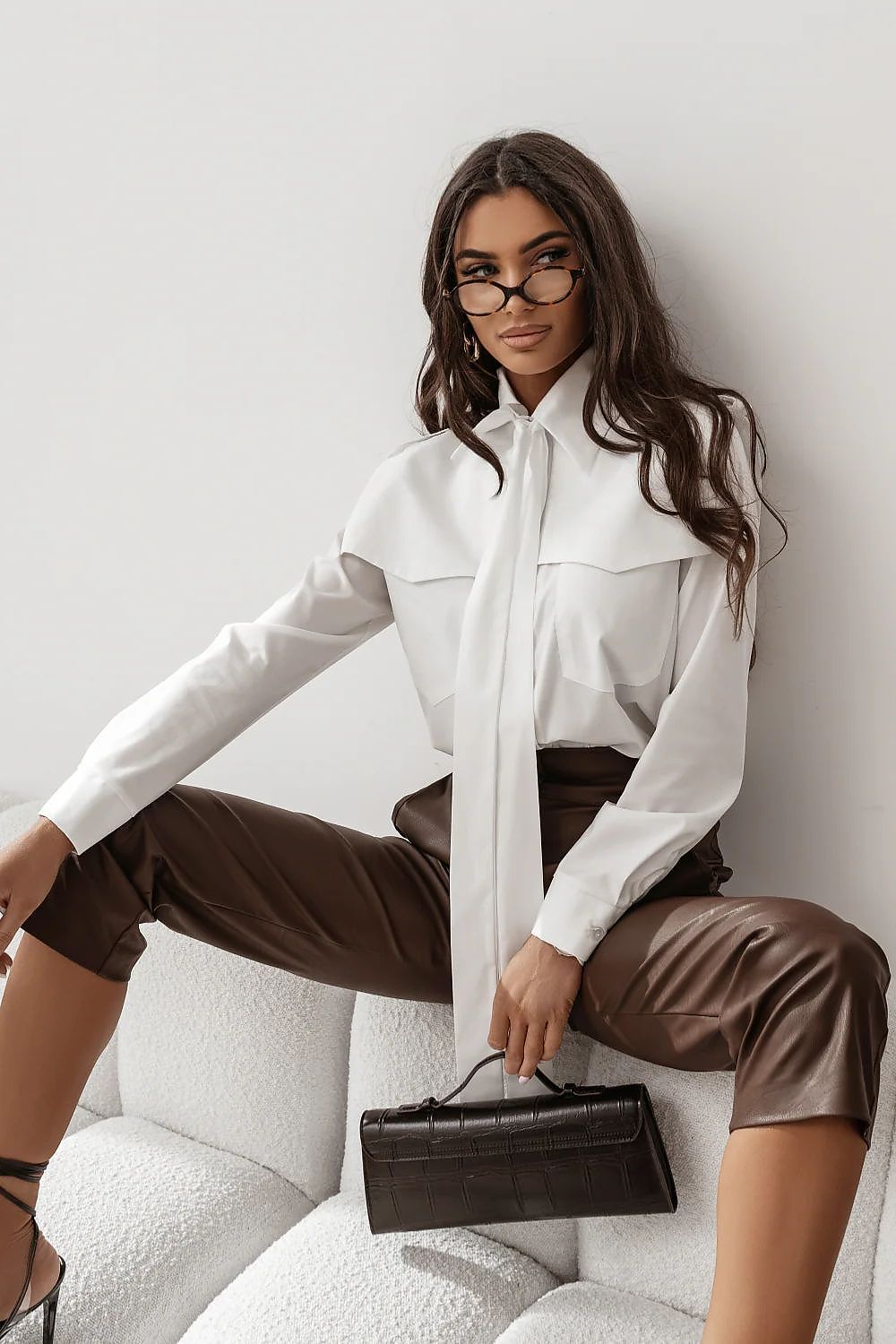  Modelo con camisa blanca de diseño vanguardista, con solapa superpuesta en los hombros y lazada en el cuello.