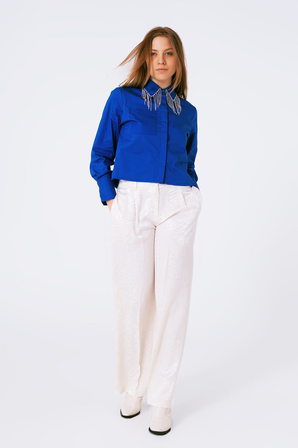 Look completo con camisa azul de flecos de brillantes y pantalones blancos.