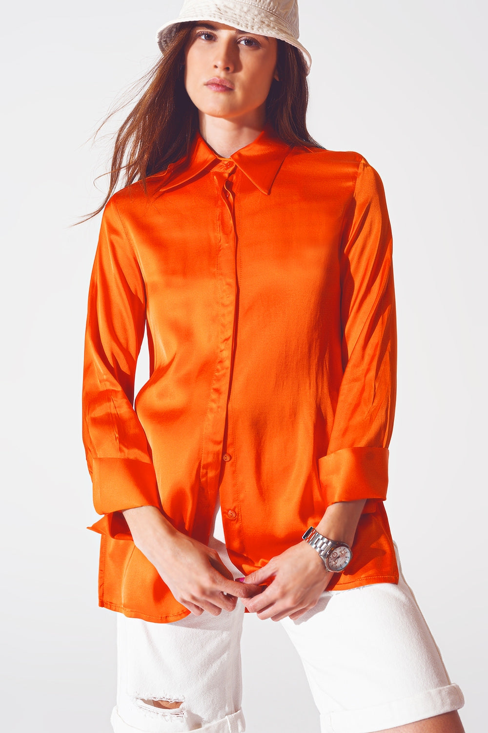 Modelo con look completo de camisa de satén naranja oversize, llevada como sobrecamisa, y bermudas blancas.