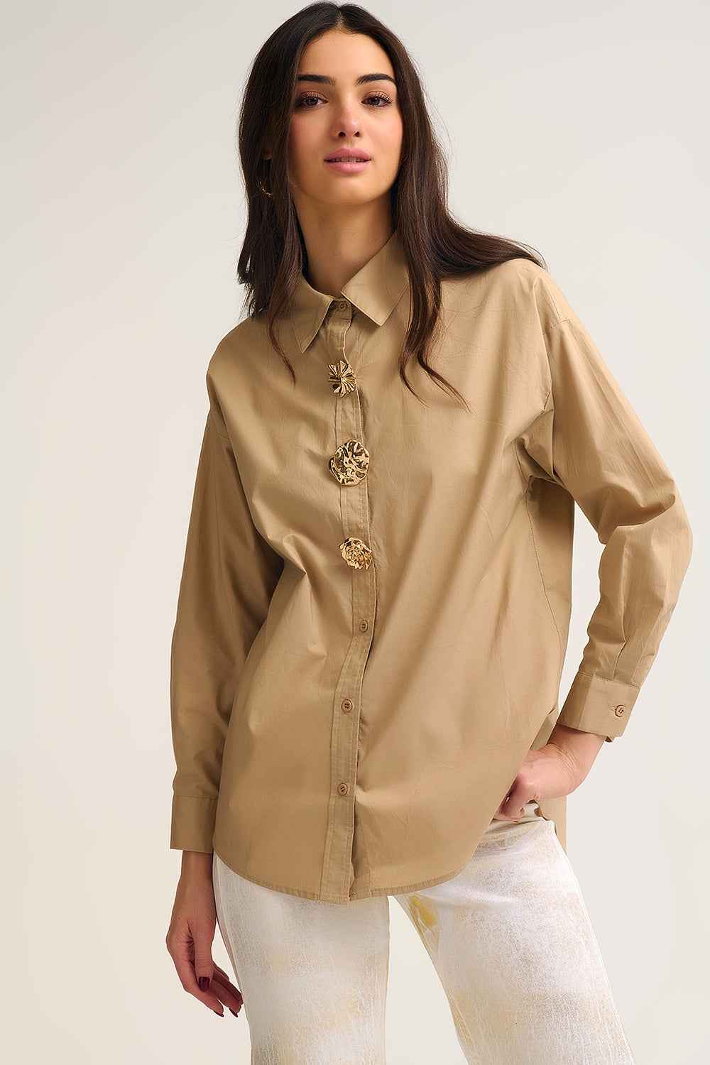 Mujer vistiendo camisa amplia de popelín beige arena 100% algodón con botones dorados grandes tipo joya.
