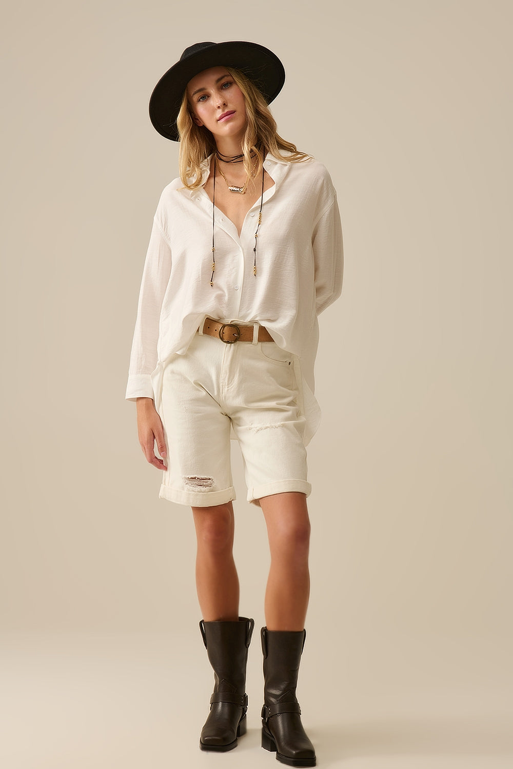 Mujer con camisa blanca relaxed fit de manga larga, detalle del cinturón camel y look monocromático elegante.
