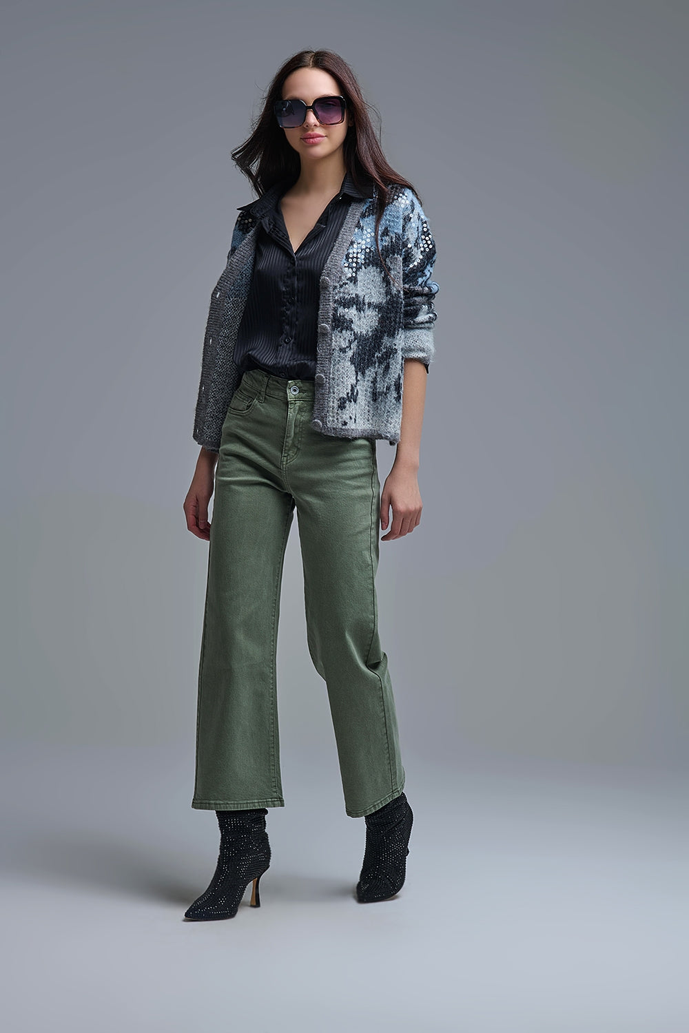 Look completo de una mujer con cárdigan de punto abstracto y lentejuelas, camisa negra y pantalón verde militar.