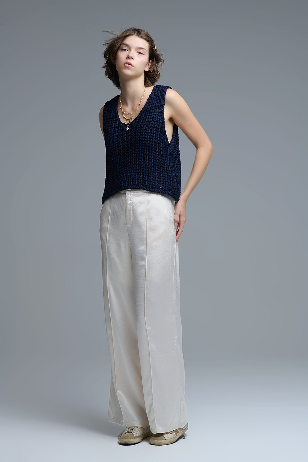 Mujer con chaleco azul marino sin mangas y pantalón blanco en look completo.