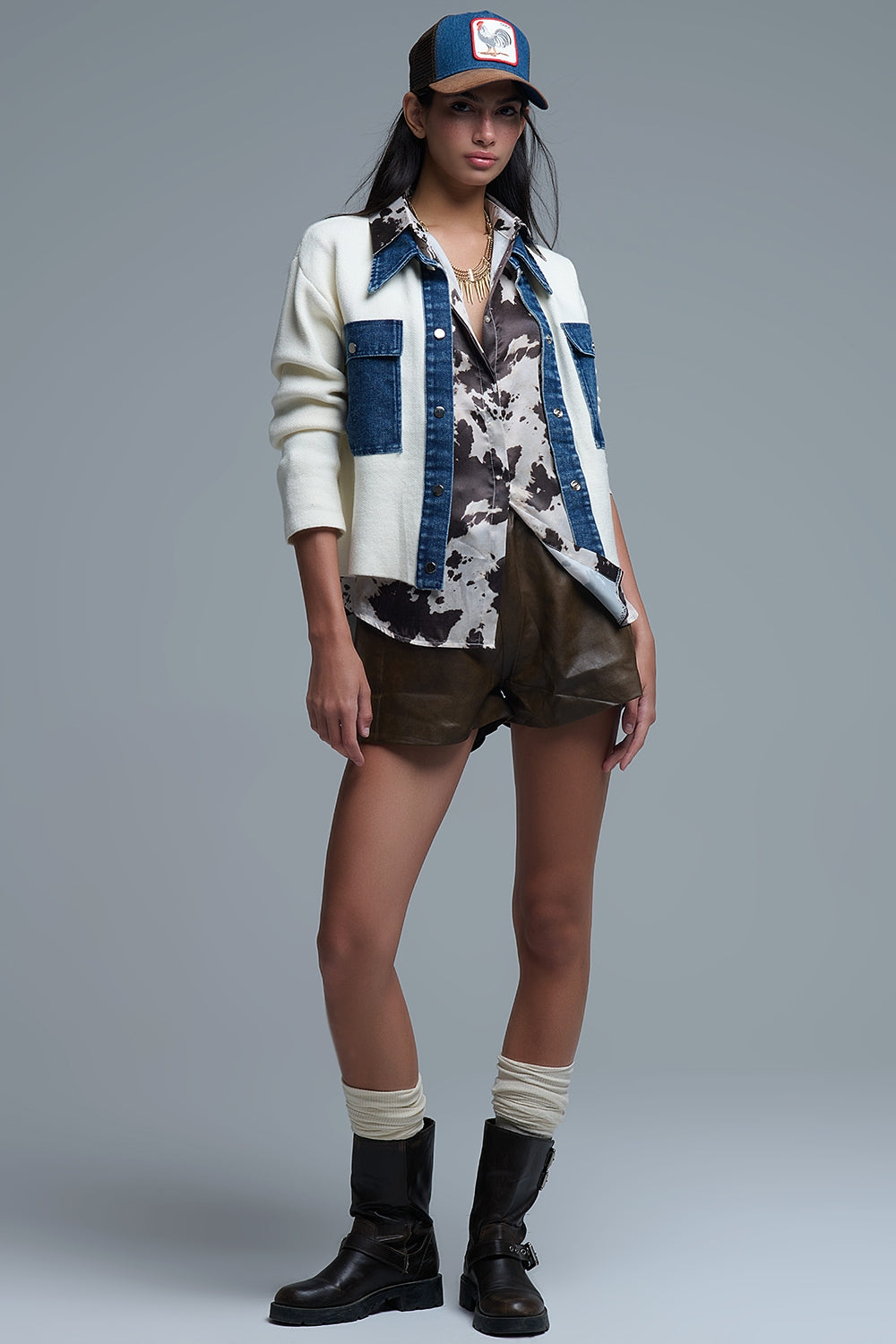 Mujer vistiendo chaqueta híbrida de punto color crema con cuello y bolsillos de tela vaquera azul, estilo casual con gorra.