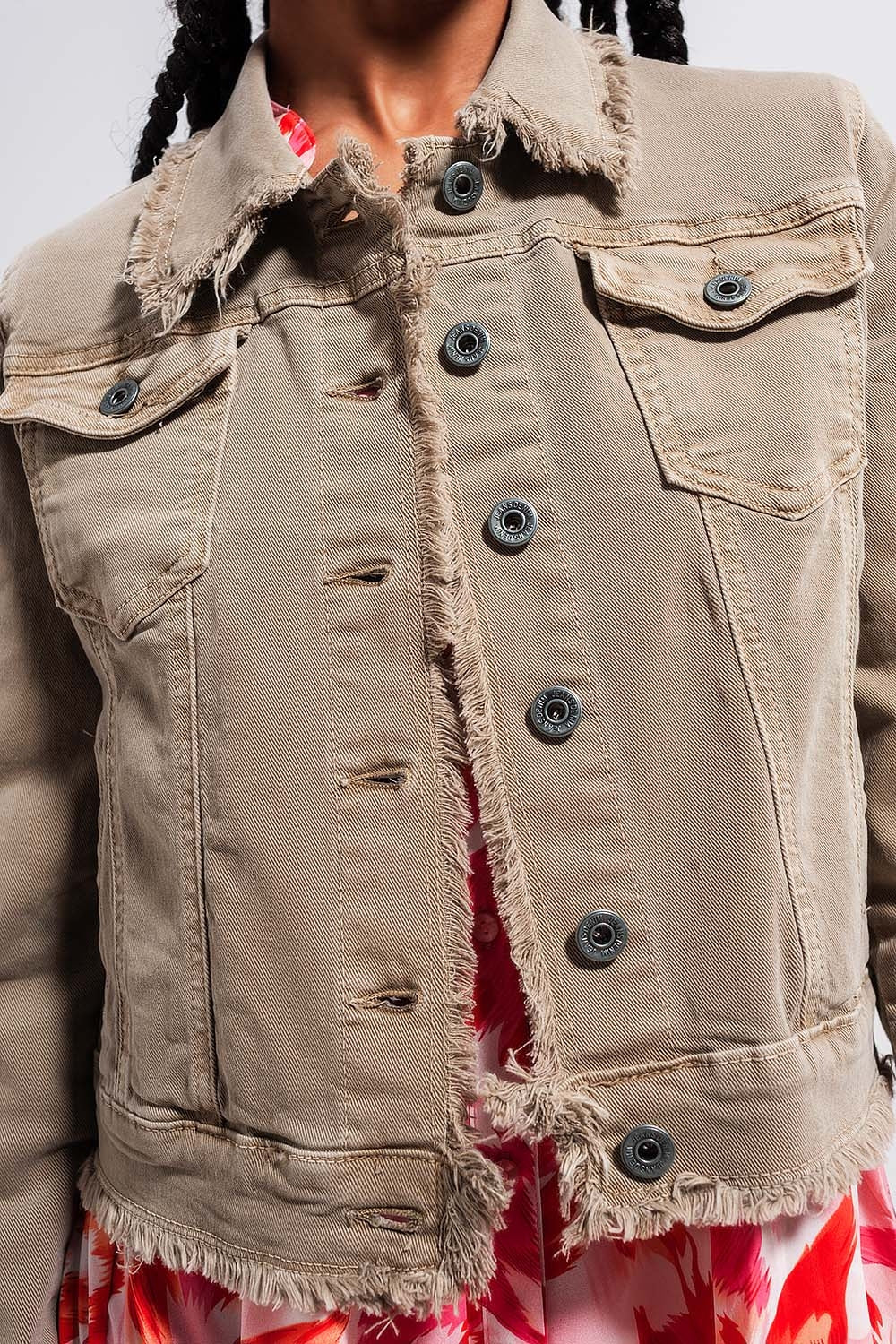 Detalle de botones metálicos y bordes deshilachados en chaqueta vaquera gris