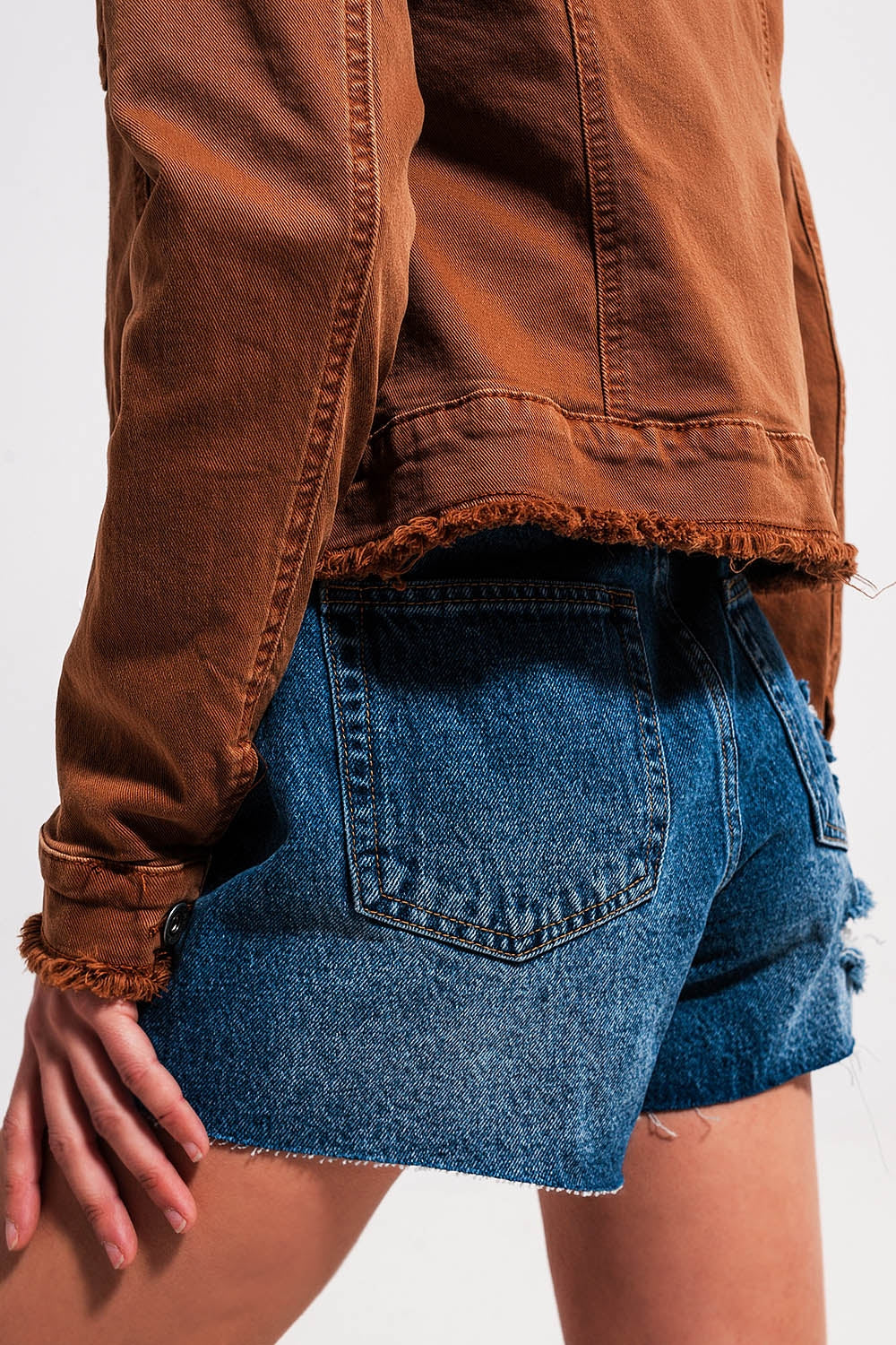 Detalle de bajo deshilachado en chaqueta vaquera marrón.