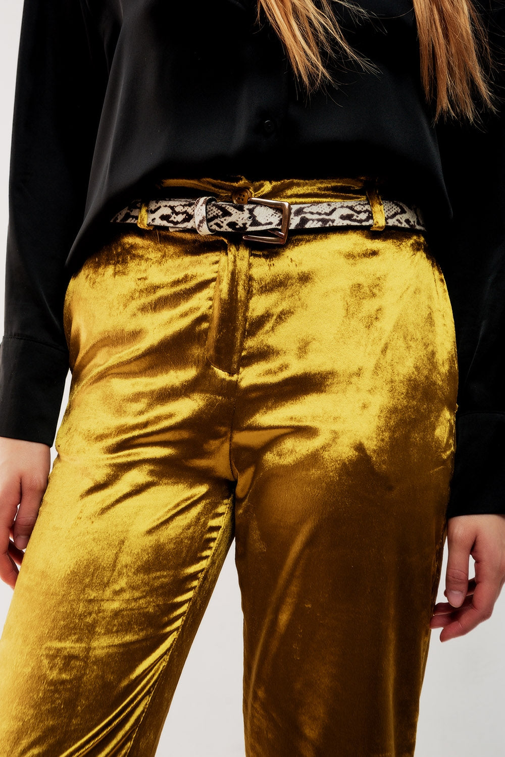 Detalle de la cintura de un pantalón de terciopelo dorado con cinturón de estampado de serpiente.