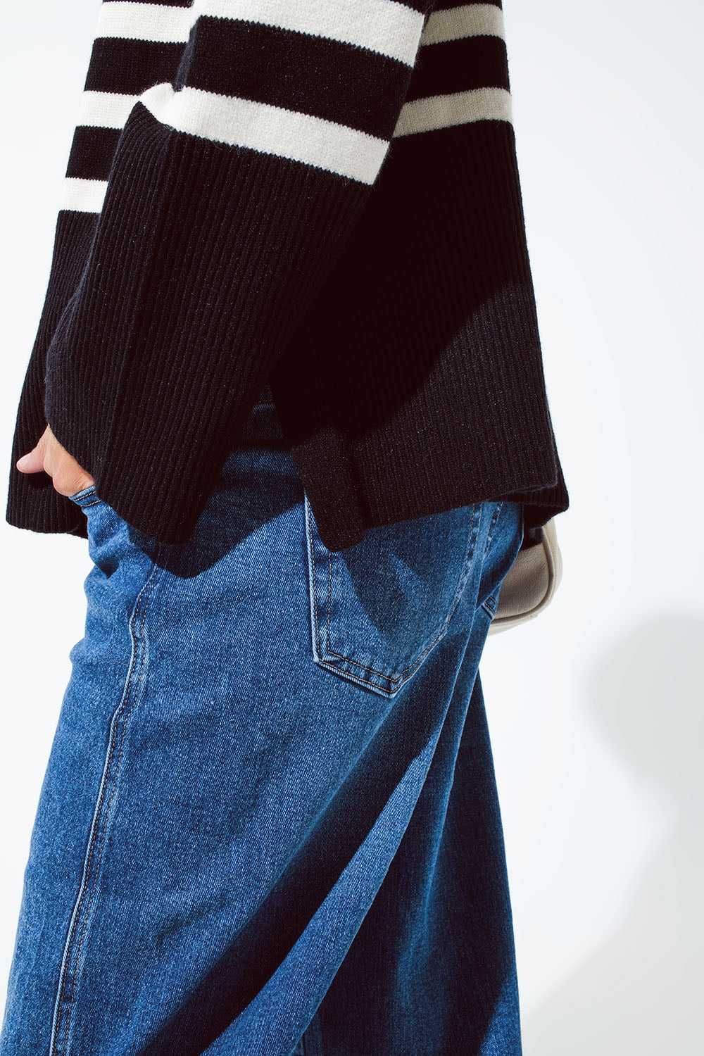 Detalle lateral de un jersey negro de rayas oversize mostrando la abertura lateral y el bajo asimétrico.
