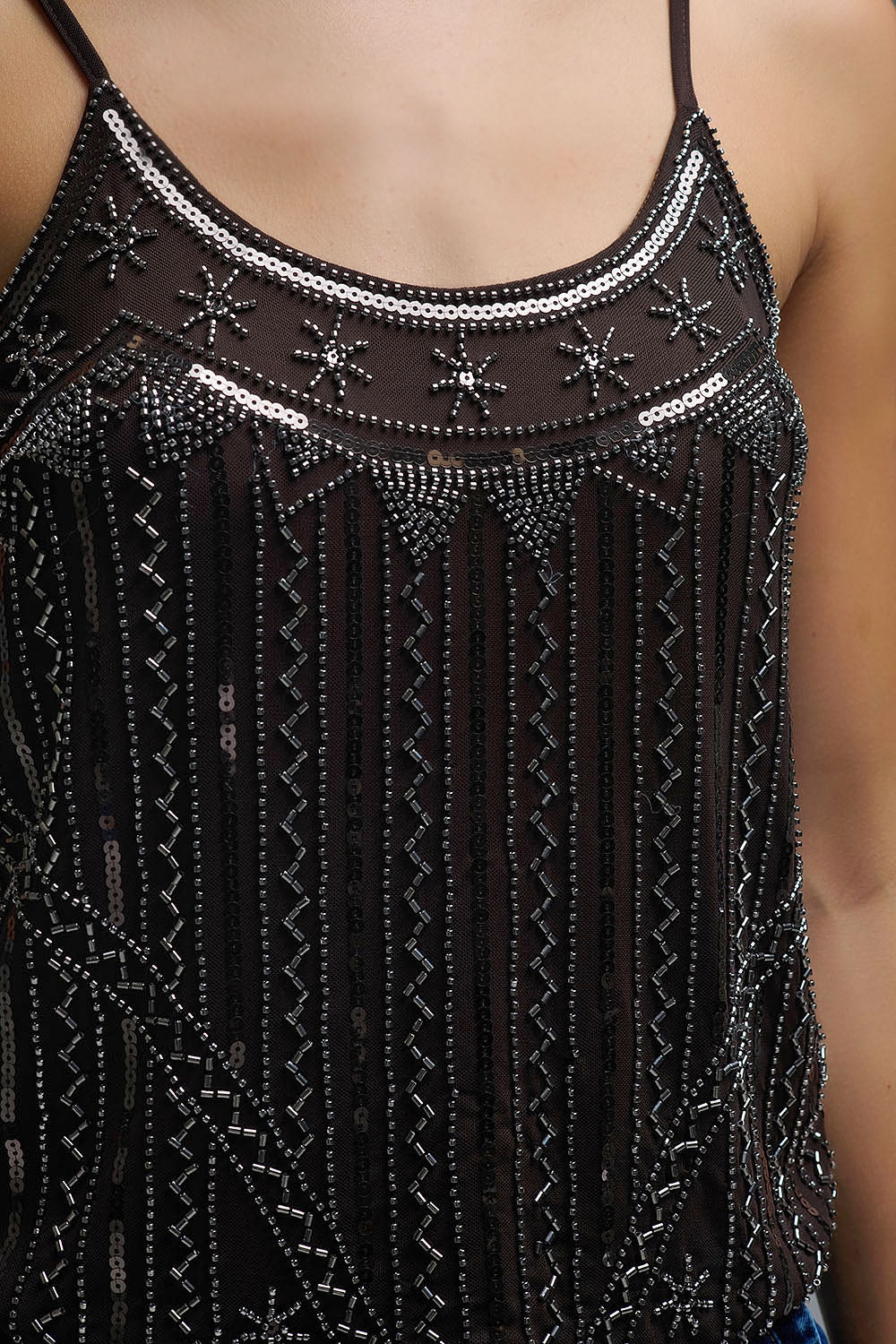 Primer plano del escote redondo con bordados geométricos de canutillos y lentejuelas sobre gasa marrón.