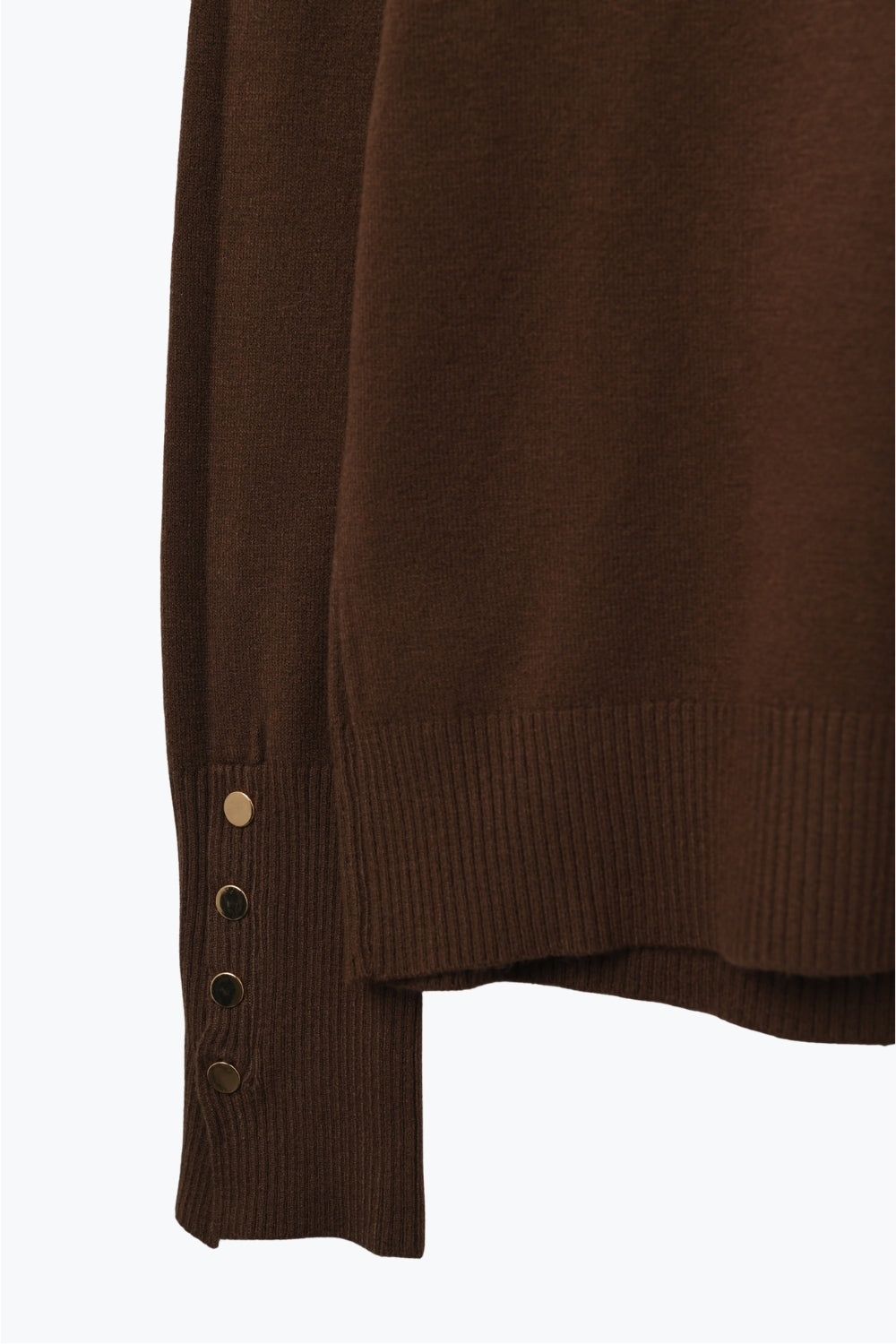 Primer plano del detalle de los botones dorados decorativos en el puño de un jersey de punto marrón.