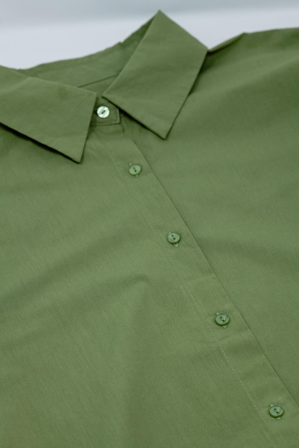 Primer plano del cuello camisero y la botonadura frontal de una blusa de popelín verde.