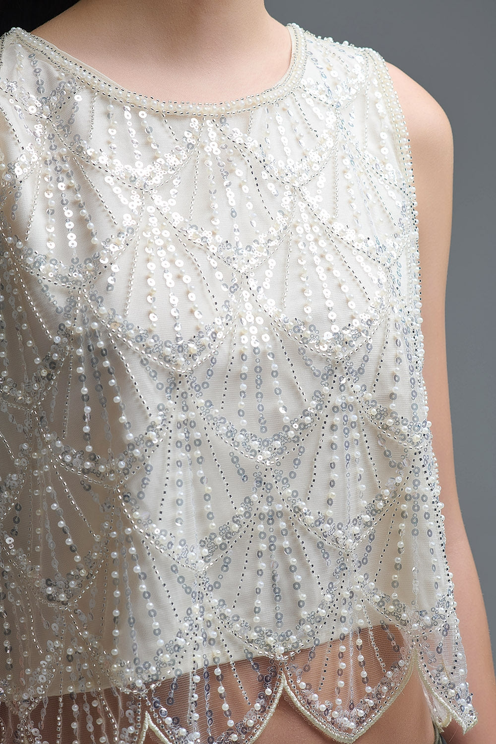 Detalle del bordado de lentejuelas y cuentas color perla estilo art déco sobre top blanco.