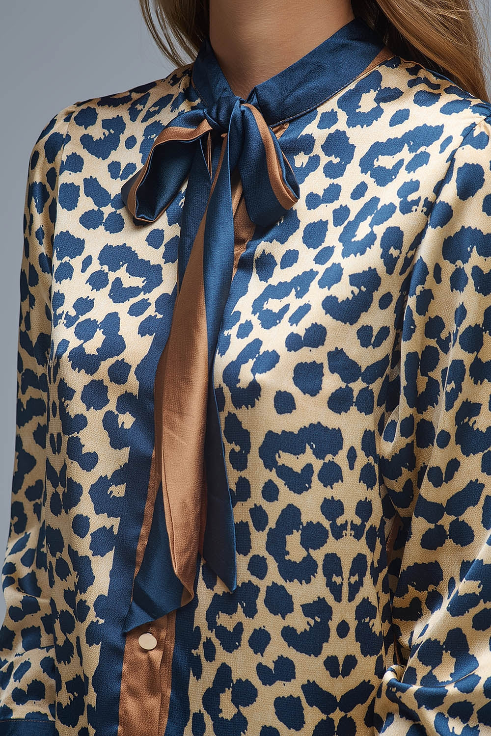 Detalle del cuello con lazo bicolor de una blusa de satén con estampado de leopardo.