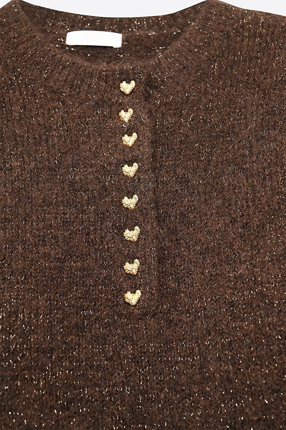 Primer plano de los botones dorados en forma de corazón en la tapeta de un jersey de punto marrón.