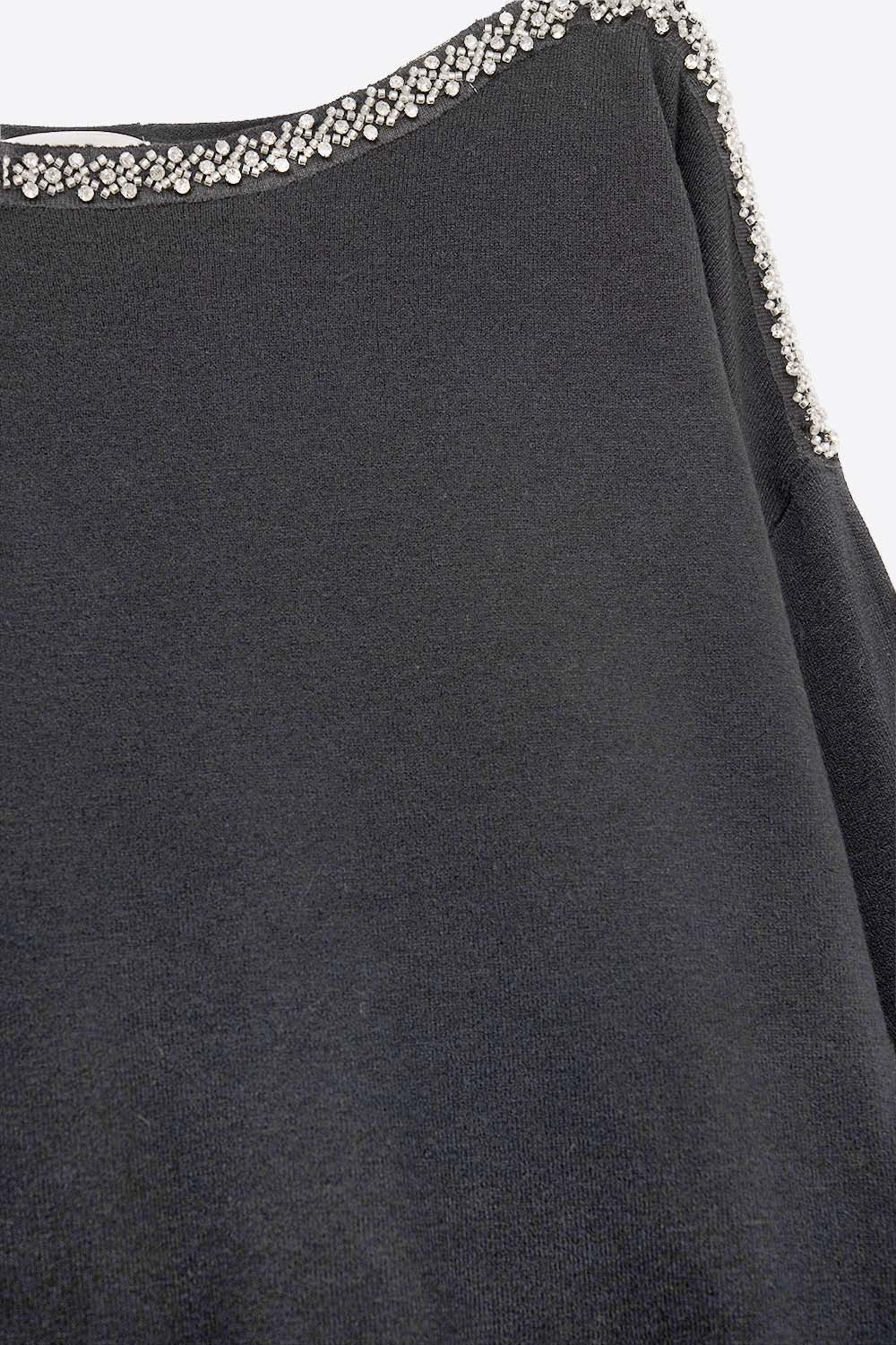 Detalle macro del bordado de strass y perlas en el cuello barco de un jersey negro de punto fino de viscosa.