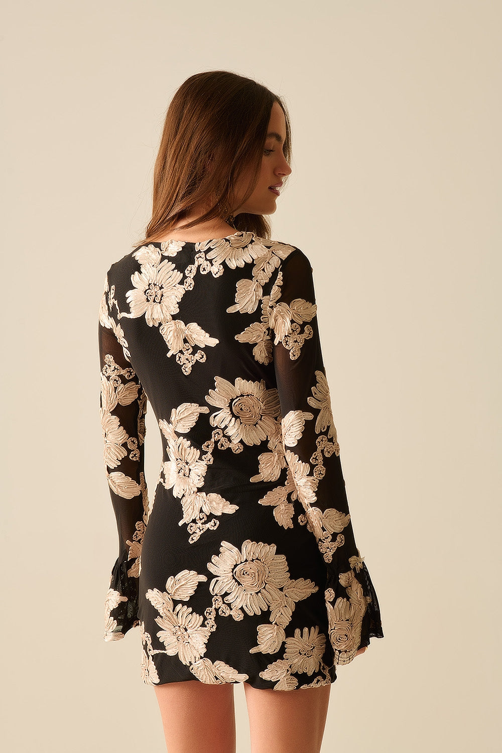 Vista trasera de un mini vestido negro bodycon con bordado floral y mangas acampanadas.