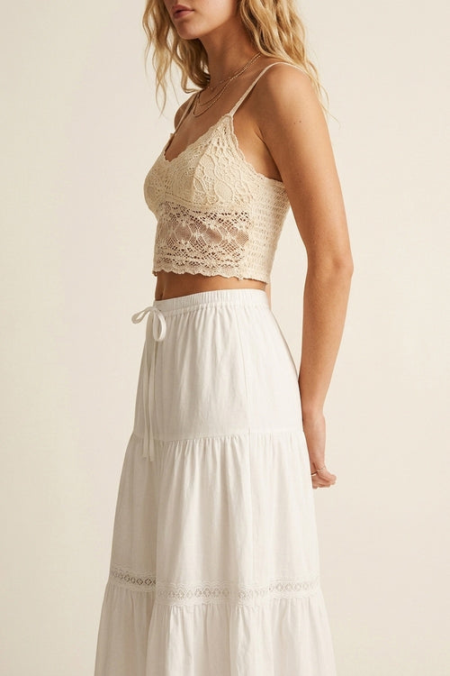 Falda larga blanca de algodón combinada con top de encaje en un estilismo veraniego mediterráneo.