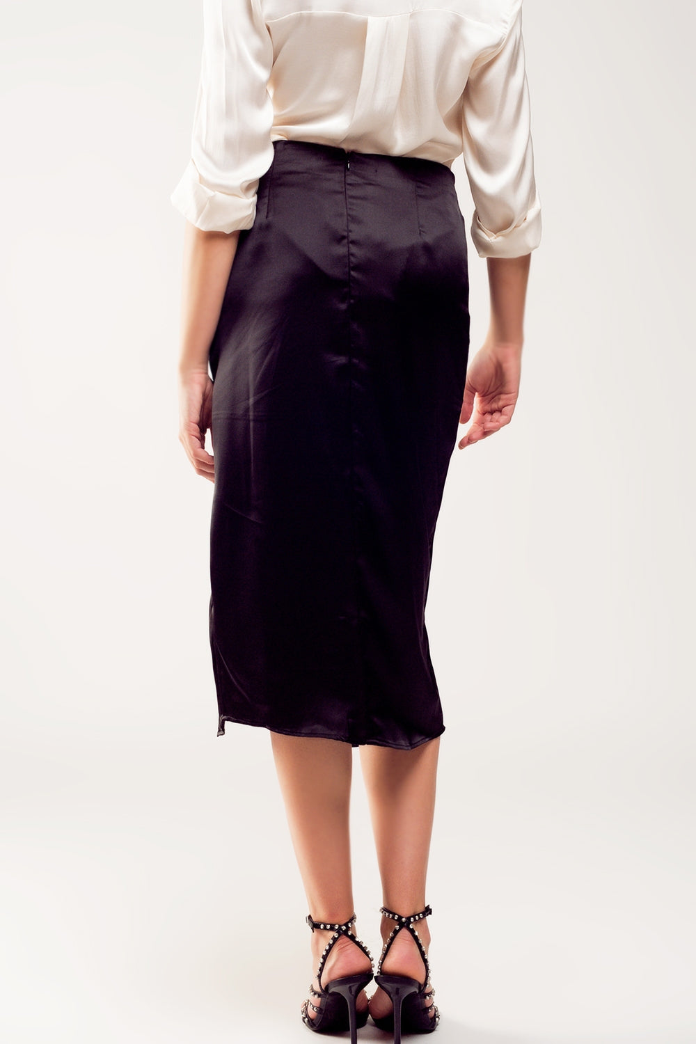 Falda midi de satén negro para mujer con abertura lateral y tres botones de pedrería, combinada con camisa blanca de seda.