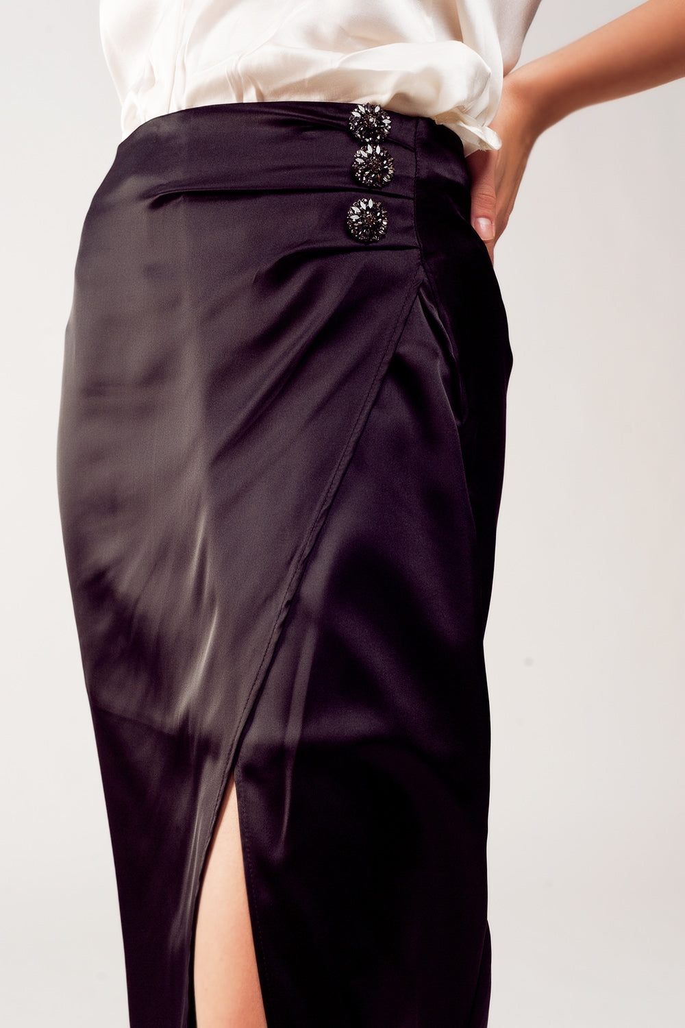 Falda midi de satén negro para mujer con abertura lateral y tres botones de pedrería, combinada con camisa blanca de seda.